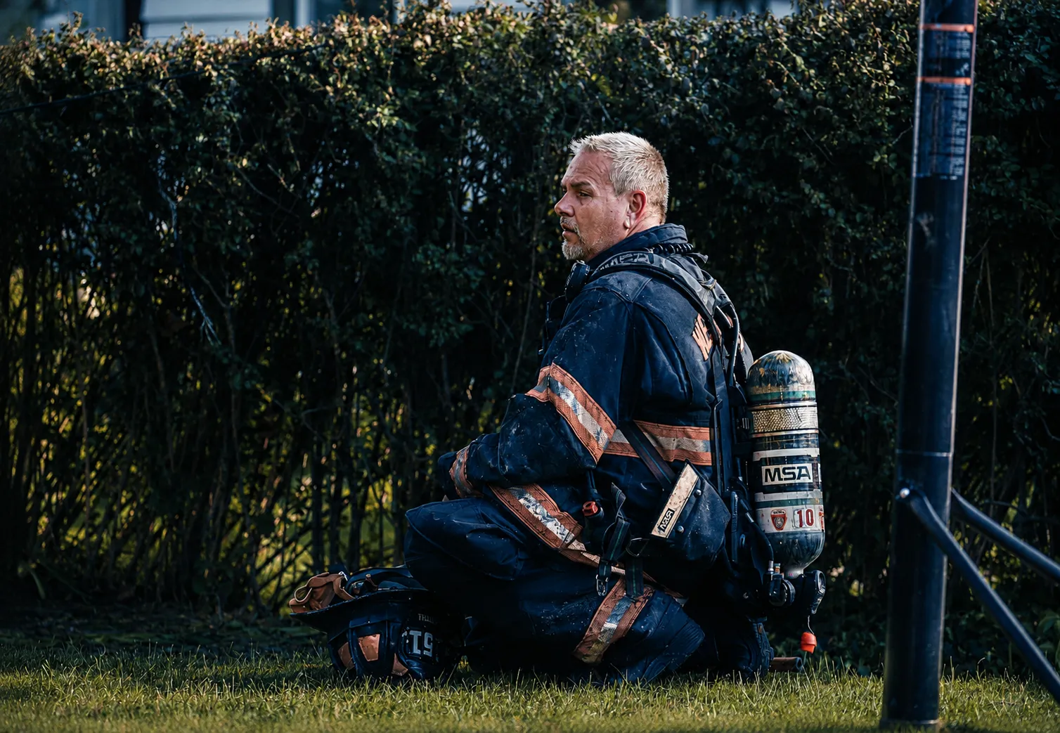 A volunteer firefighter in full turnout gear kneeling after a call, the community service roots behind TK’s Towing