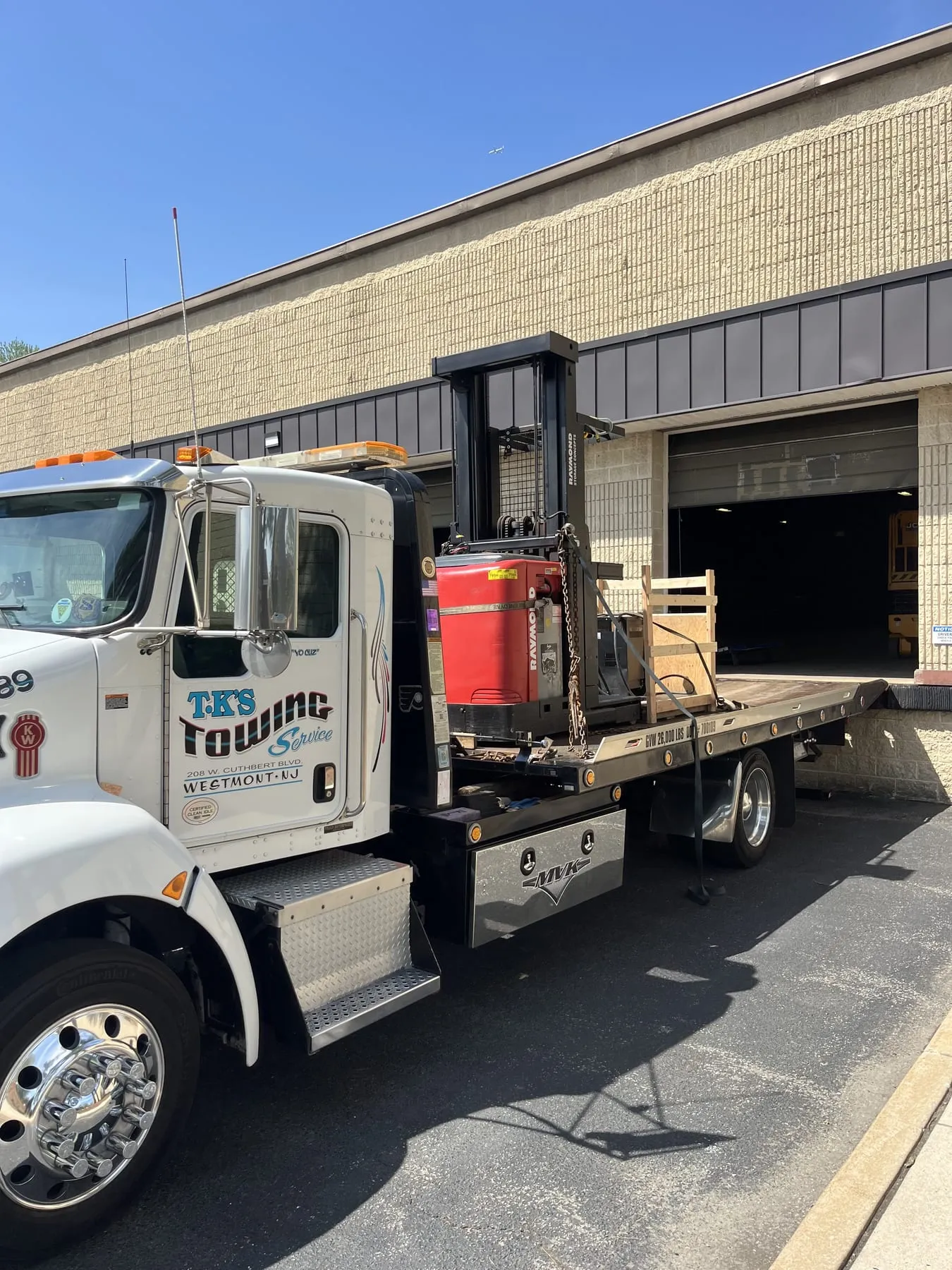 A forklift loaded on the TK's Towing flatbed at a loading dock