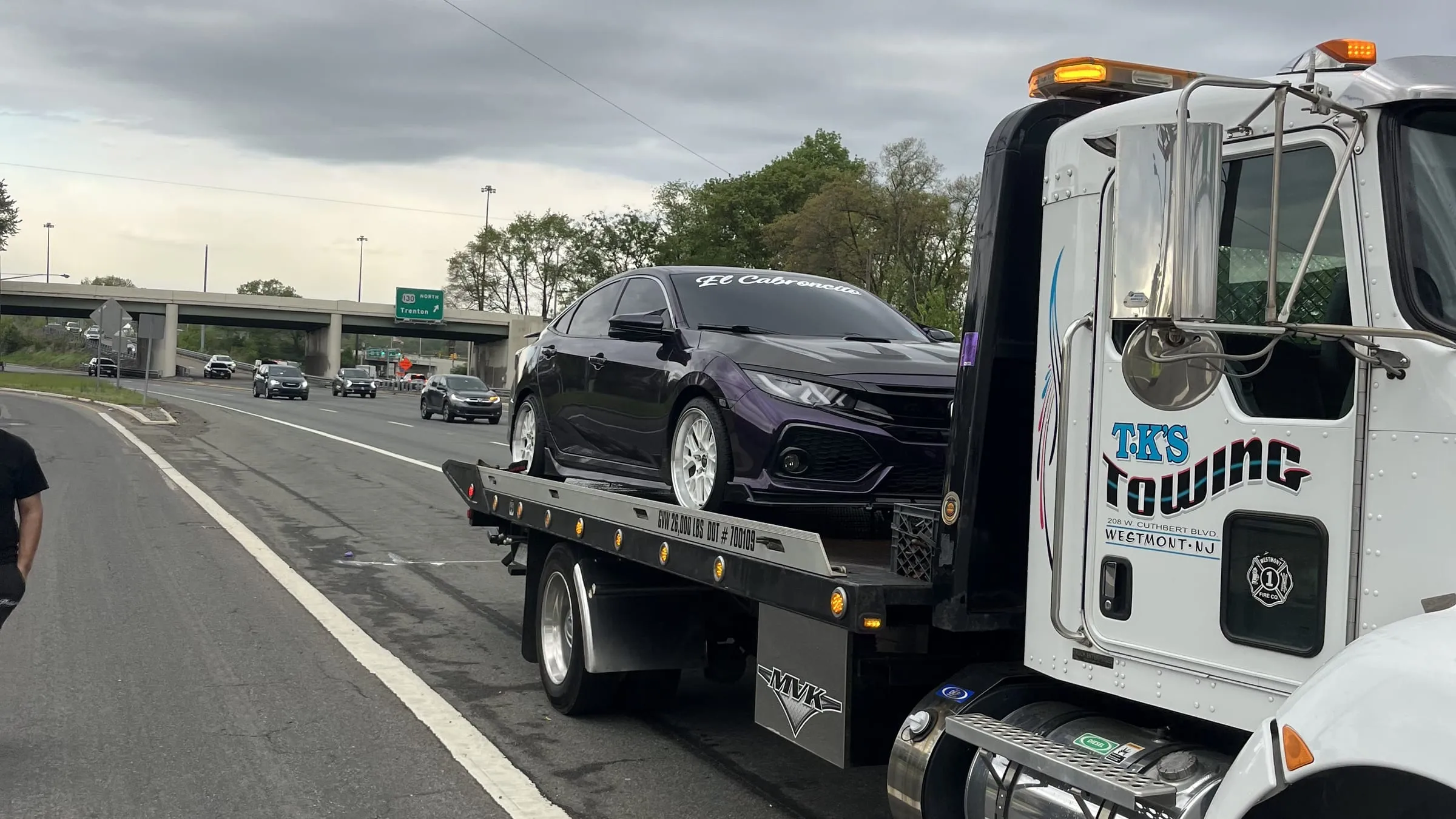 A sedan loaded on the TK's flatbed on the highway shoulder
