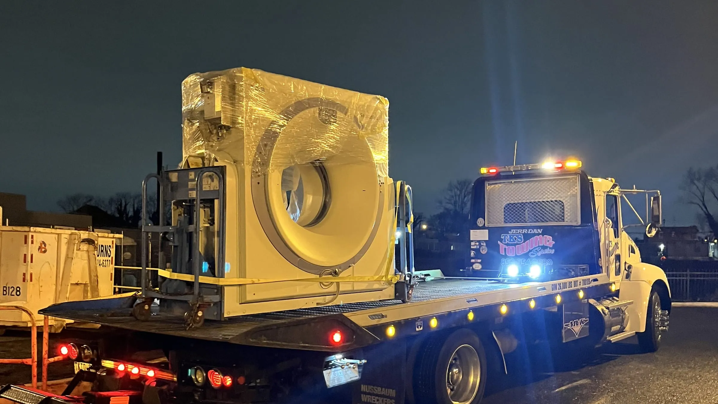 Large medical equipment strapped to the TK's flatbed at night under the truck's work lights